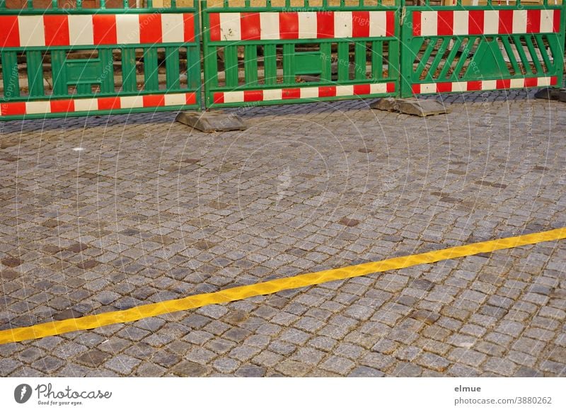 grüne Absperrbaken mit rot-weißen Streifen am Straßenrand und eine gelbe Fahrbahnbegrenzung auf der gepflasterten Straße / Fahrbahneinengung / Baustelle