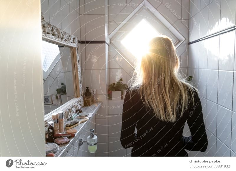 Rückansicht einer Blonden Frau, die in Bad steht blond Gegenlicht Badezimmer Sonnenlicht Pflege Hygiene im Innenbereich Fliesen u. Kacheln Farbfoto