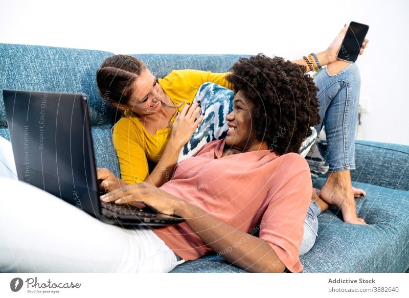 Fröhlich multirassischen lesbischen Paar mit Gadgets Chillen auf Sofa Frauen zu Hause Apparatur ruhen Spaß haben Zusammensein Kälte Partnerschaft Liebe Freundin