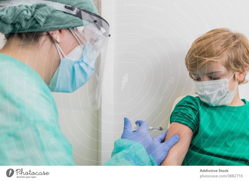 Arzt gibt Injektion für Kind in Maske im Krankenhaus Impfstoff Coronavirus Einspritzung Spritze verhindern Bund 19 steril Gesundheitswesen medizinisch COVID