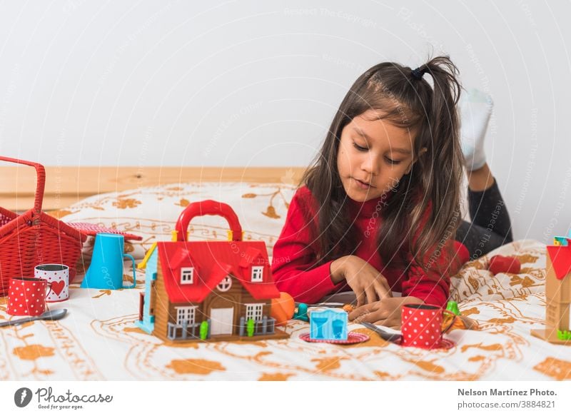 Süßes kleines Mädchen in rotem T-Shirt- Pullover mit langem Hals, das im Schlafzimmer mit seinem Spielzeug spielt. Feiertag Weihnachten Spielen Kindheit