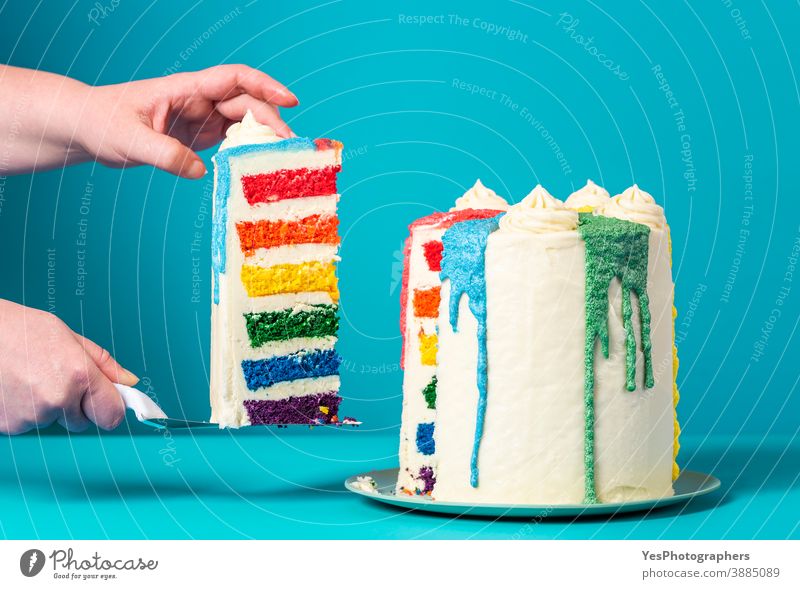 Frau nimmt sich ein Stück Kuchen. Hausgemachter Regenbogenkuchen auf blauem Hintergrund Bäckerei Geburtstag Geburtstagstorte Blauer Hintergrund Buttercreme