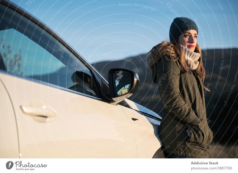 Frau steht auf der Straße in der Nähe von Auto und genießt das Wetter genießen Sonne warme Kleidung PKW ruhig sorgenfrei kalt Saison Automobil Fahrbahn Glück