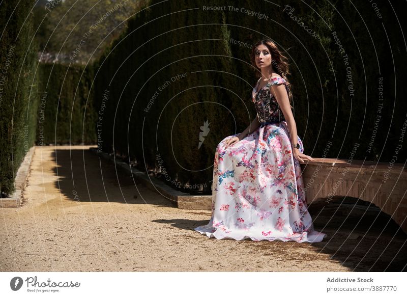 Junge Frau in langen stilvollen Kleid im Park elegant maxi Anmut langes Kleid Stil charmant Garten Bank Gasse sich[Akk] entspannen sitzen Stein traumhaft