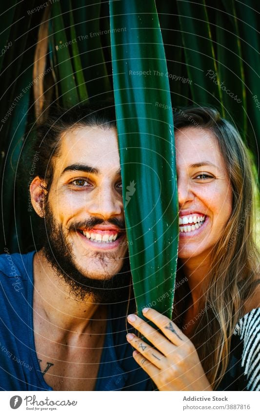 Positives Paar im tropischen Garten schaut in die Kamera Spaß haben heiter Tierhaut Pflanze Blatt Lachen unterhalten spielerisch multiethnisch