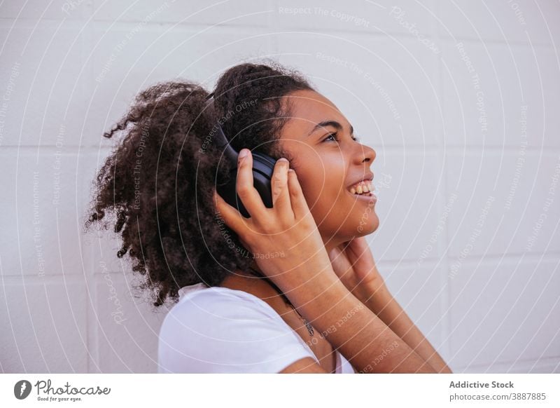 Entzückte junge Frau, die mit Kopfhörern Musik hört zuhören Gesang genießen Drahtlos Straße zufrieden Klang ethnisch schwarz Afroamerikaner heiter Apparatur