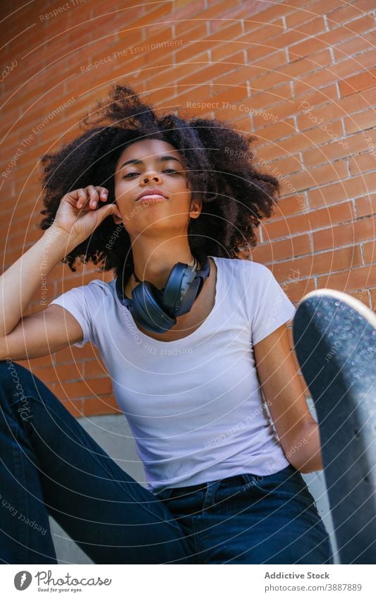Freudige schwarze Frau mit Skateboard auf der Straße urban Großstadt Wochenende Kopfhörer heiter jung Afro-Look Frisur ethnisch Afroamerikaner krause Haare
