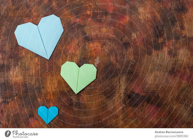 Origami-Herzen aus farbigem Papier zur Gratulation zum Valentinstag für verliebte Paare, auf altem Holzuntergrund in Brauntönen Holzplatte grün hölzern