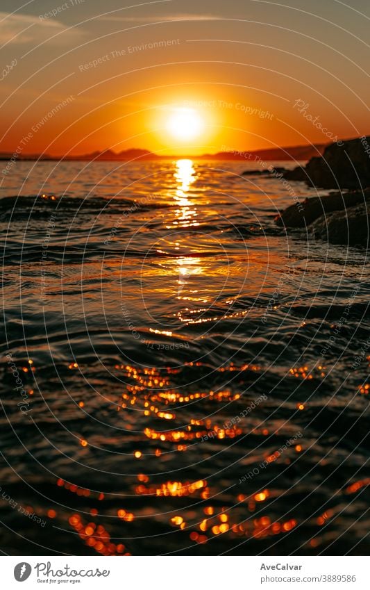 Nahaufnahme des Meeres durch die Felsen an der Küste mit einem massiven orangefarbenen Sonnenuntergang über den Inseln als Hintergrund Ruhe Gutschein geistig