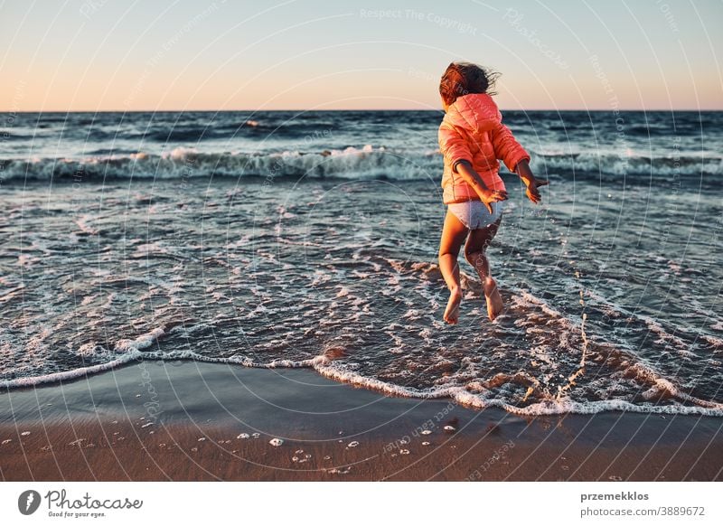 Verspieltes kleines Mädchen, das bei Sonnenuntergang am Sandstrand über die Meereswellen springt aufgeregt frei genießen positiv Emotion sorgenfrei Natur