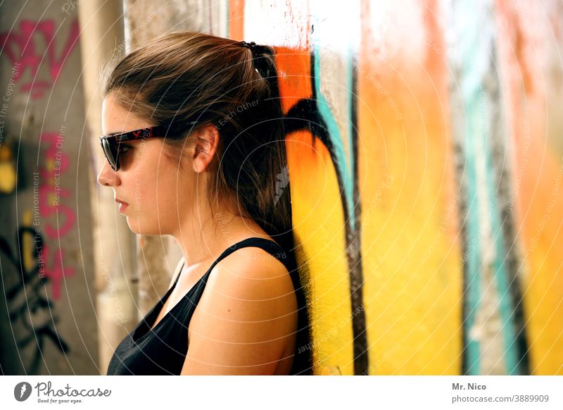 Teenager lehnt entspannt an einer Grafittiwand Graffiti Wand Mauer Mädchen Sonnenbrille Porträt Haare & Frisuren Blick authentisch orange feminin Coolness