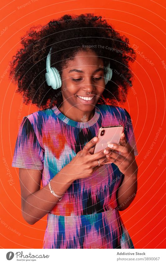 Fröhliche schwarze Frau mit Smartphone und Kopfhörer Musik Model hell benutzend Stil modern tausendjährig Selfie Atelier Apparatur zuhören lebhaft Inhalt lässig