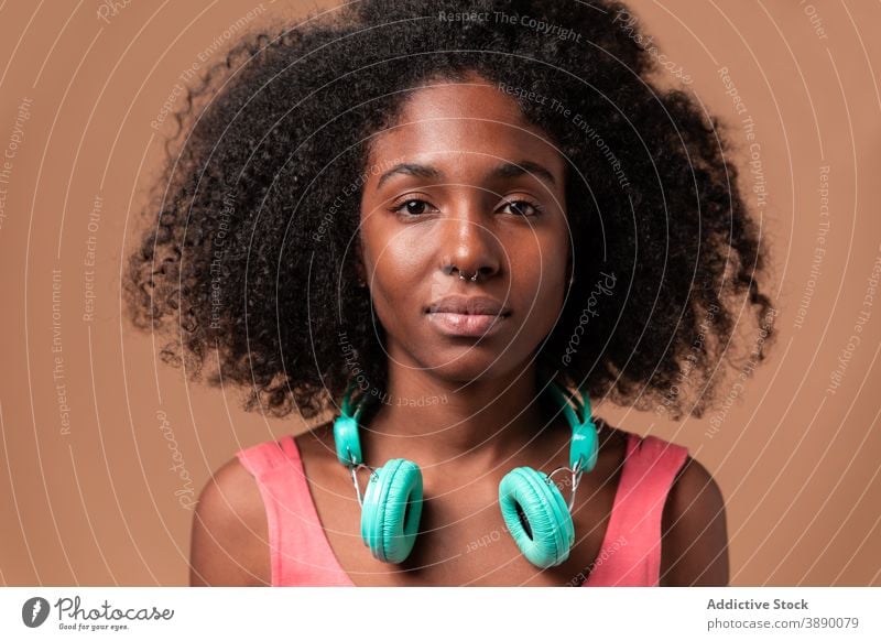 Ethnische Frau mit Kopfhörern im Studio stehend Spaß Musik Stil Atelier farbenfroh Frisur Afro-Look ethnisch Kubaner Afroamerikaner schwarz Lächeln trendy Kleid