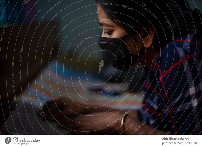 Eine indische junge Frau mit Corona-Präventionsmaske, die zu Hause mit einem Laptop auf dem Bett liegt - 19. 19. Indischer Lebensstil und Krankheit. Erwachsener