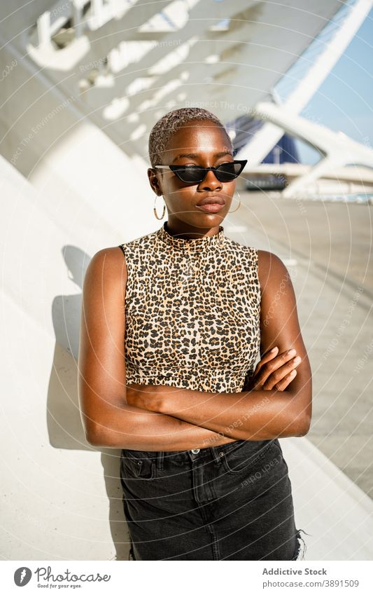 Ernste schwarze Frau steht auf der Straße ethnisch Afroamerikaner cool Sonnenbrille Stil urban jung trendy expressiv Kleidungsstück hell Individualität Geflecht