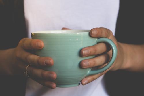 Nahaufnahme einer großen hellgrünen Tasse mit Kaffee oder Tee in den Händen einer jungen Frau. Becher halten festhalten schwarz weiß Getränk Teetasse