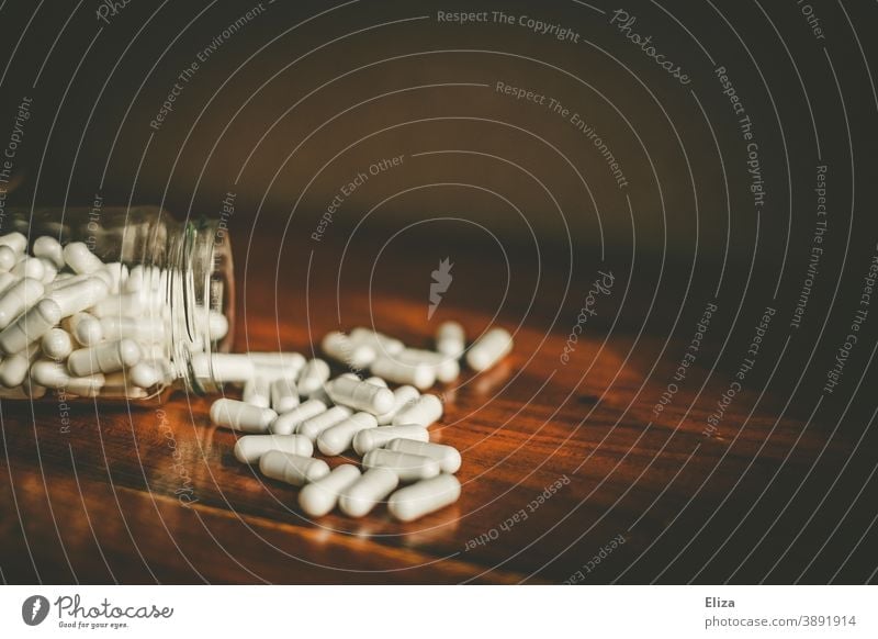 Ein Glas aus dem sich viele weiße Medikamentenkapseln auf einen Tisch ergießen Pillen Medizin Tablette Kapsel Arzneimittel Meidkament Tabletten Vogel Behälter