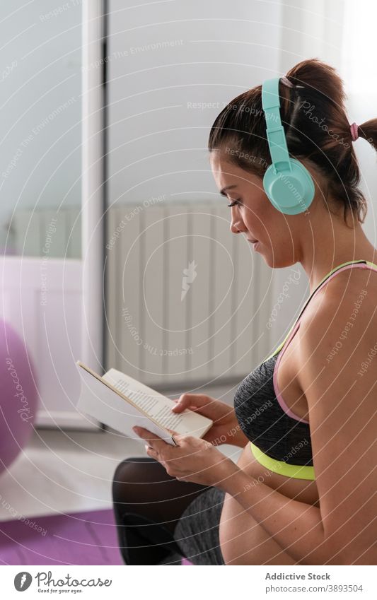 Schwangere Frau streckt Körper und Lesen Buch während Yoga-Praxis schwanger Dehnung lesen zuhören Musik multitask Schwangerschaft Sportkleidung erwarten