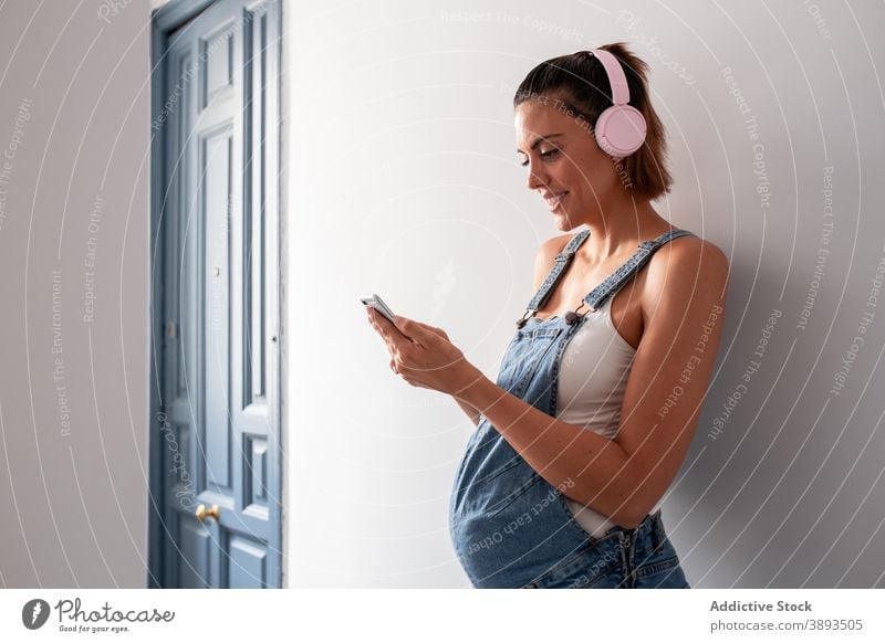 Schwangere Frau genießt Musik in Kopfhörer zu Hause schwanger zuhören Schwangerschaft gesamt genießen Gesang Drahtlos Lächeln heiter Raum Melodie Klang