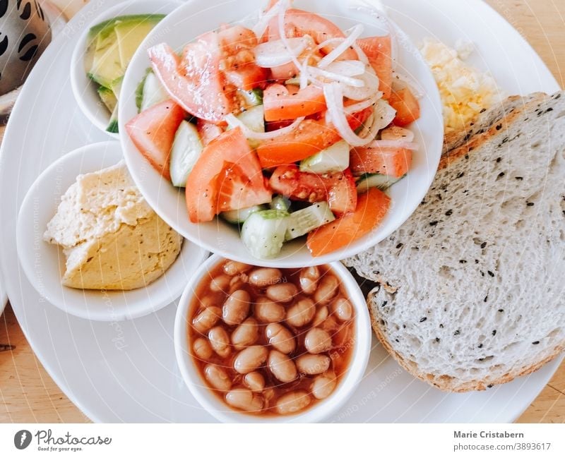 Ansicht von oben: Vollkornbrot, Bohnen, Avocado, Hummus, veganer Käse und Kokosnussjoghurt mit Kaffee für ein vollwertiges und gesundes veganes Frühstück