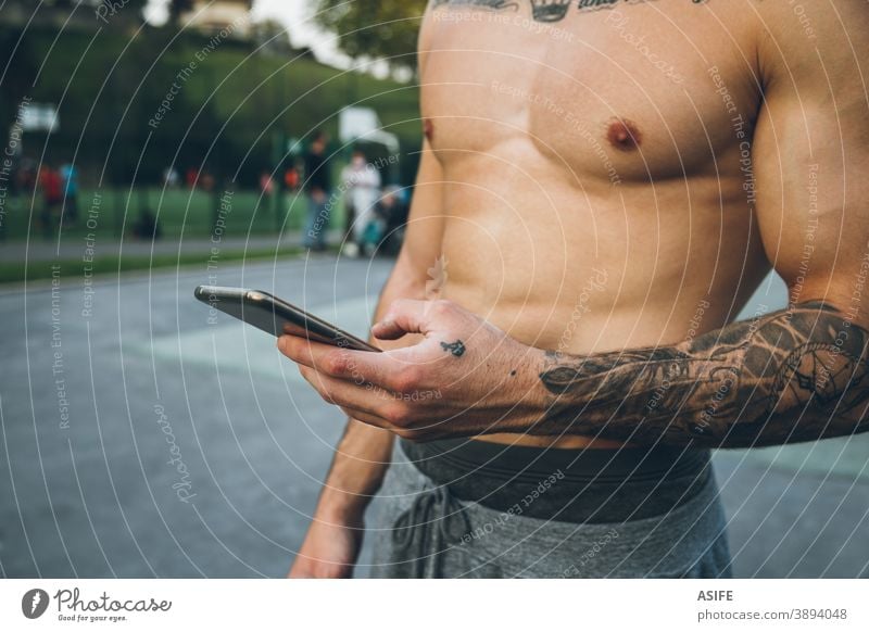 Junger städtischer Bodybuilder mit Tätowierungen, der sein Smartphone während des Gymnastiktrainings benutzt Hände Athlet Mann Muskeln Handy Telefon Arme Tattoo