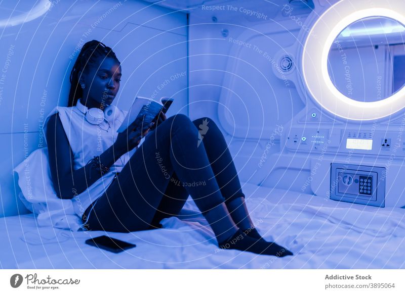 Frau mit Buch, die sich in einem Kapselhotel ausruht Hotel Bett lesen ruhen Reisender Unterkunft sich[Akk] entspannen jung Afroamerikaner schwarz ethnisch