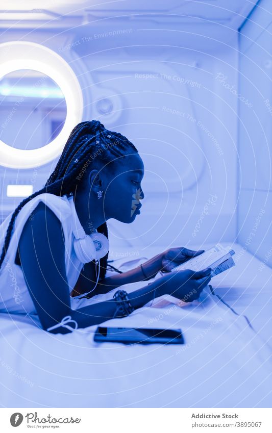 Junge schwarze Frau liest Broschüre im Kapselhotel Hotel Bett lesen ruhen Reisender Unterkunft sich[Akk] entspannen Prospekt jung Afroamerikaner ethnisch