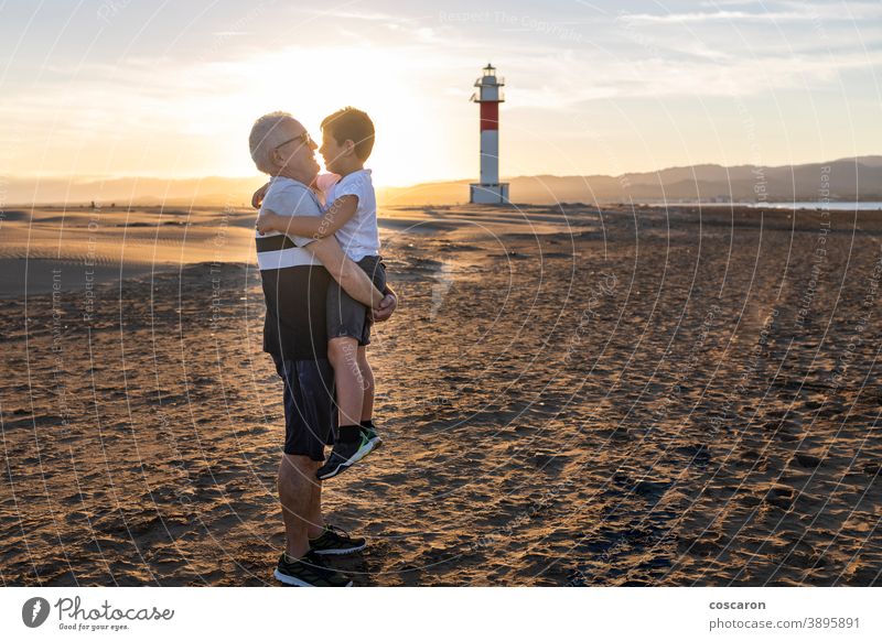 Großvater und Enkel umarmen sich an einem Strand mit einem Leuchtturm im Hintergrund Rücken Junge Kind Kindheit Kinder Küste Papa Tag älter Familie Fangar