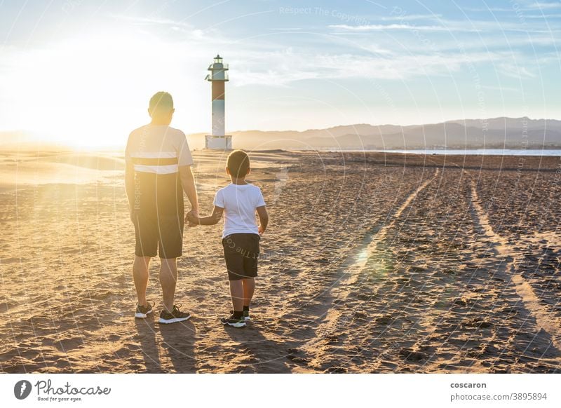 Großvater und Enkel schauen bei Sonnenuntergang auf einen Leuchtturm am Strand Rücken Junge Kind Kindheit Kinder Küste Papa Tag älter Familie Fangar