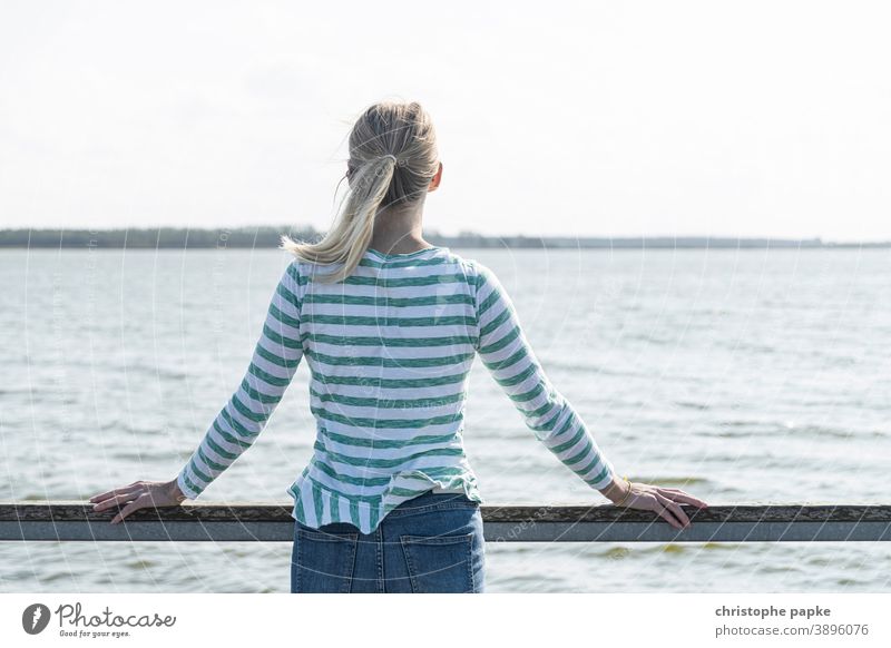 Blonde Frau steht an Rehling und blickt aufs Meer blond Rückansicht Urlaub Ostsee Bodden Boddenlandschaft Mecklenburg-Vorpommern entspannen ausblick genießen