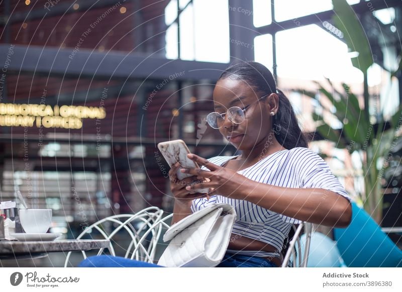 Ethnische Frau entspannt in Café auf Smartphone Tee Teekanne ruhen sorgenfrei Apparatur Gerät ethnisch schwarz Browsen Handy Afroamerikaner Kälte Tisch