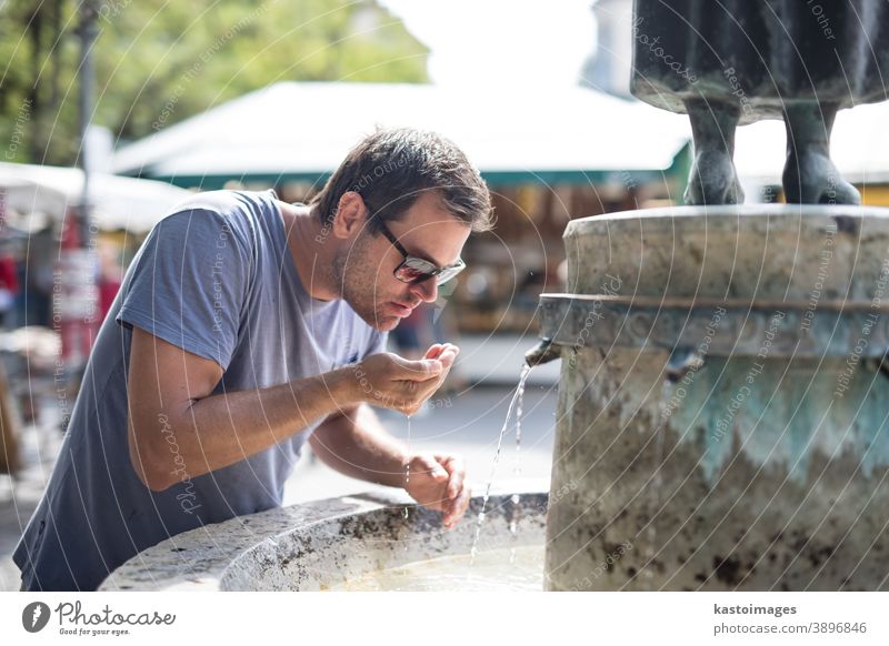 Durstiger junger, ungezwungener Kucasier trinkt an einem heißen Sommertag Wasser aus einem öffentlichen Stadtbrunnen Springbrunnen Hydrat Mann durstig