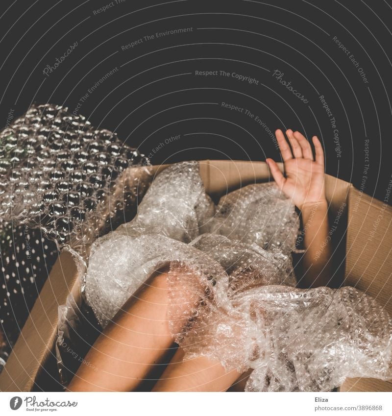 Mensch in einem Karton, Gliedmaßen gucken zwischen Verpackungsmaterial aus Plastik heraus nackt Paket Versandkarton Menschenhandel Plastikfolie Ware Mensch