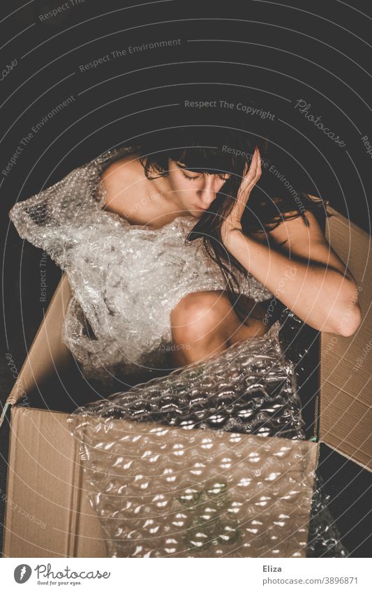 Frau sitzt in einem Karton zwischen Verpackungsmaterial aus Plastik Kiste Mensch Plastikfolie Müll Kunststoffverpackung Versandkarton nackt Geschenk Paket
