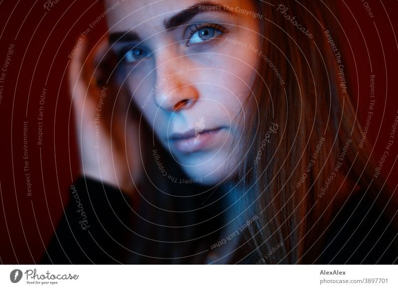 Portrait einer jungen Frau in einem Raum vor roter Wand mit rotem und blauem Licht Studentin anmutig Gesichtsausdruck Empathie Blick in die Kamera