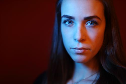 Portrait einer jungen Frau in einem Raum vor roter Wand mit rotem und blauem Licht Studentin anmutig Gesichtsausdruck Empathie Blick in die Kamera