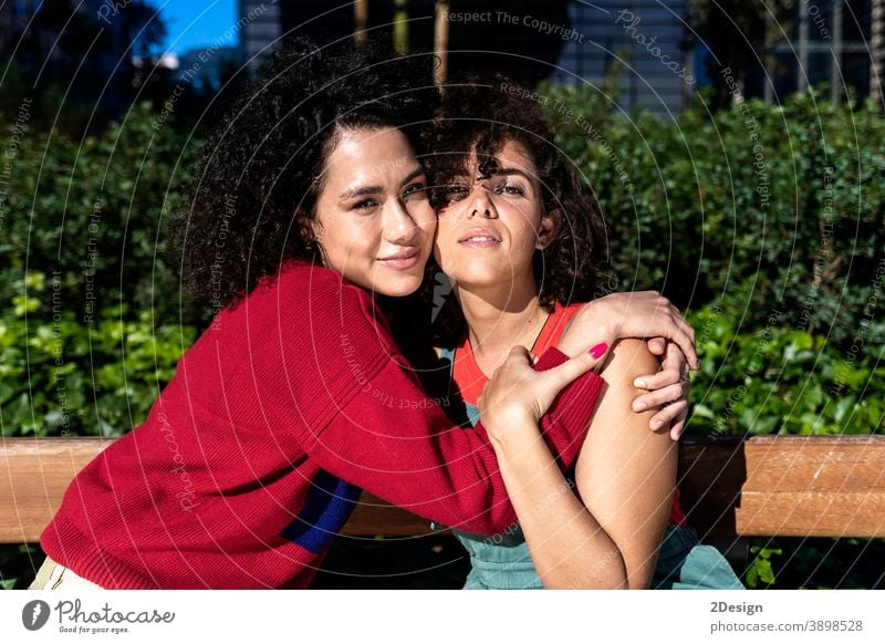 Lächelndes lesbisches Paar, das sich auf einer Parkbank umarmt und entspannt anhänglich Nähe umarmend ethnisch Ethnizität Freunde Freundschaft Lachen Liebhaber