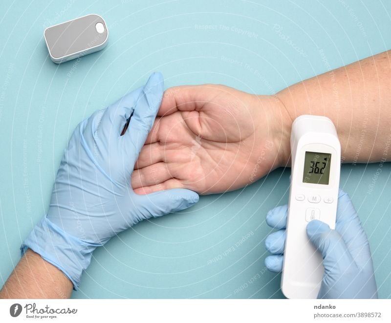 Arzt in blauen Latexhandschuhen misst die Temperatur mit einem elektronischen kontaktlosen Gerät Pulsoxymeter Prüfung Thermometer Werkzeug Behandlung Virus weiß