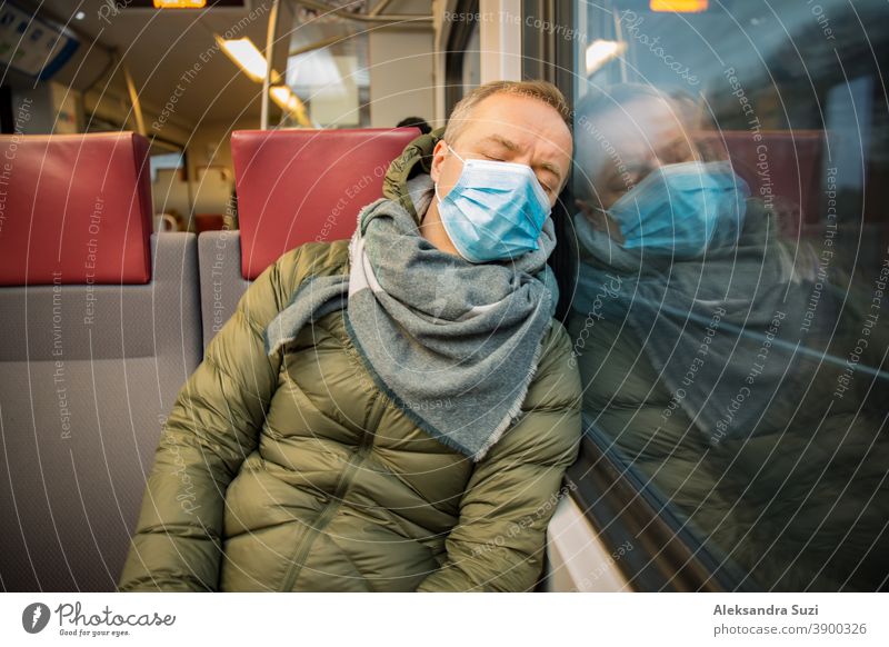 Reisen in öffentlichen Verkehrsmitteln während der Pandemie. Ein müder Mann mittleren Alters mit einer medizinischen Schutzmaske auf dem Gesicht schläft im Nahverkehrszug.