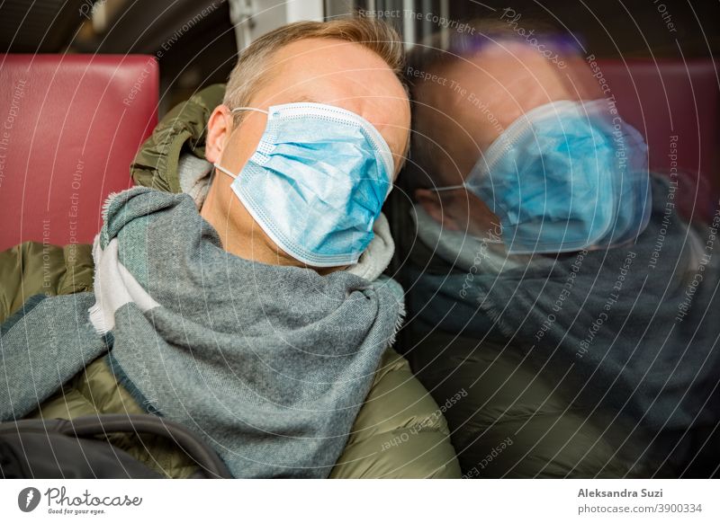 Reisen in öffentlichen Verkehrsmitteln während der Pandemie. Ein müder Mann mittleren Alters mit einer medizinischen Schutzmaske auf dem Gesicht schläft im Nahverkehrszug.