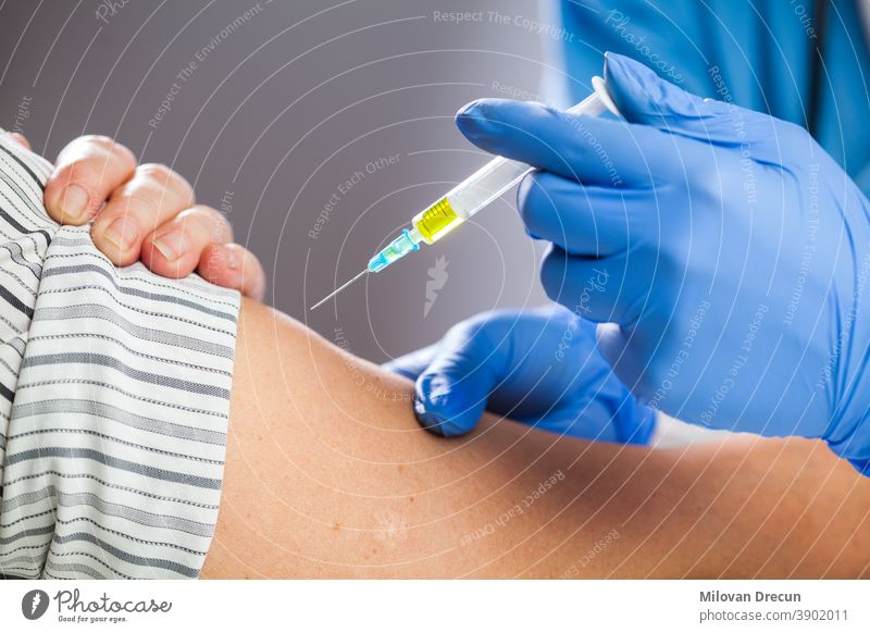Coronavirus-COVID-19-Immunisierungskonzept,medizinisches Personal mit blauen Latexschutzhandschuhen, das eine mit gelber Flüssigkeit gefüllte Spritze hält,Impfstoffdosis an den Patienten verabreichen,Nahaufnahme der kaukasischen Hand