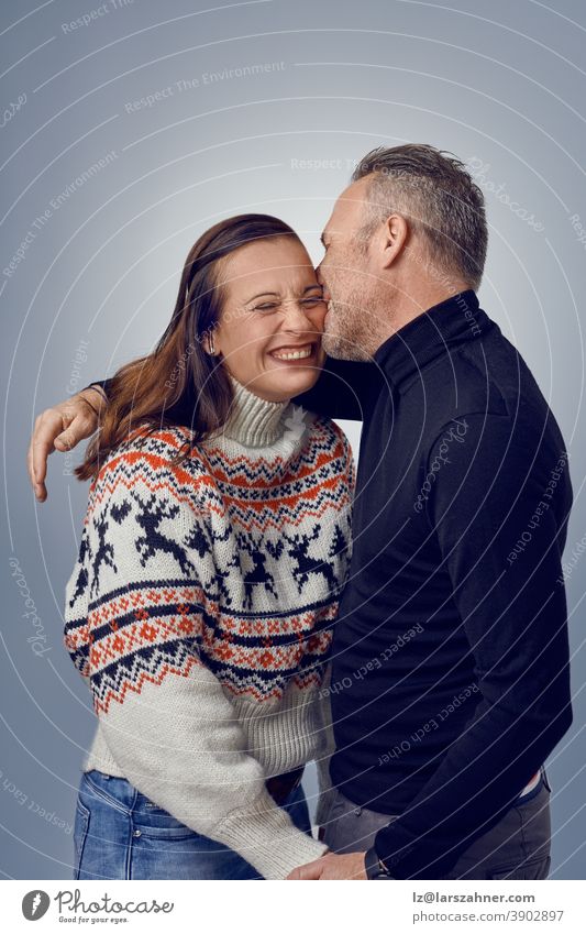 Erwachsene Mann küsst seine glückliche lachende Frau. Loving Paar in warmen Pullover posieren für Familienporträt. Winterurlaub Fotoshooting Konzept im Studio