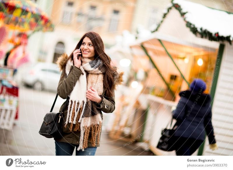 Fröhliche Modefrau benutzt im Winter auf dem Weihnachtsmarkt ein Smartphone auf der Straße attraktiv schön Weihnachten neu Jahr Funktelefon Großstadt Gerät Frau