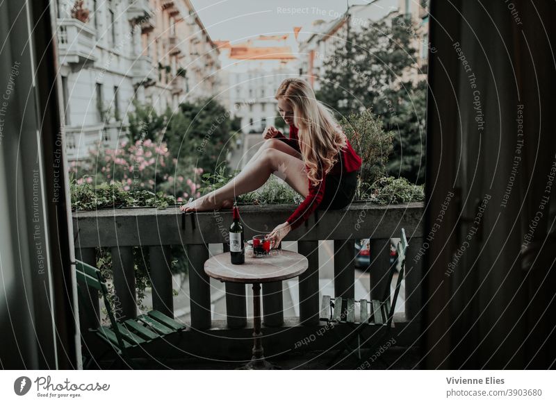 Frau sitzt auf einem Balkon und trinkt Wein trinken lange Haare langhaarig Alkoholsucht Sitzen Weinflasche Farbfoto Außenaufnahme Single Quarantäne Alleine Zeit