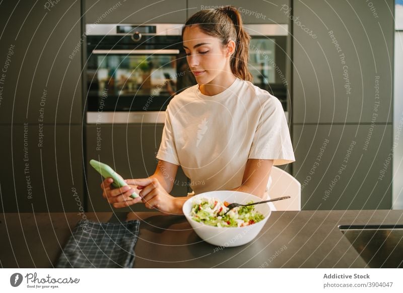 Frau beim Mittagessen und Surfen auf dem Smartphone zu Hause Salatbeilage Browsen Gemüse gesunde Ernährung Küche soziale Netzwerke lesen Nachrichten Internet