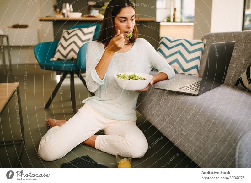 Junge Frau isst Salat und schaut Video auf Laptop zuschauen essen zu Hause Salatbeilage Gesundheit jung Apparatur Lebensmittel lässig Lifestyle Internet online