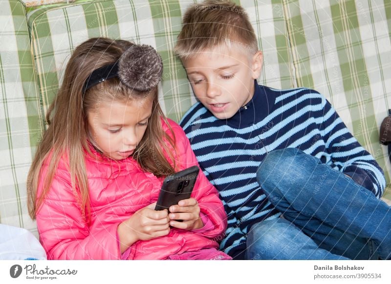 Mädchen sitzt auf einer Schaukel und spielt Handyspiele auf dem Smartphone. Junge sitzt neben ihr und macht sich Sorgen über den Prozess des Spielens Freund. Bild mit selektivem Fokus