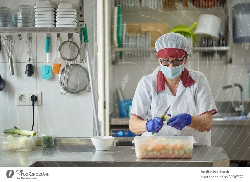 Koch mit Schutzmaske und Handschuhen bei der Zubereitung von Speisen in der Küche Coronavirus Mundschutz vorbereiten Frucht Lebensmittel behüten geschnitten