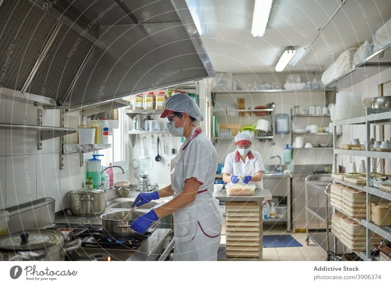 Küchenpersonal mit Masken und Handschuhen beim Kochen von Speisen Coronavirus vorbereiten Lebensmittel Mundschutz behüten Arbeit Pandemie Kollege Mitarbeiterin