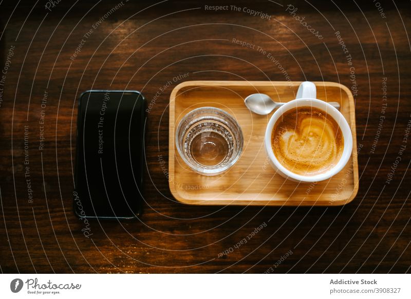 Tasse Kaffee und Glas Wasser in der Nähe des Smartphones platziert Mobile Telefon trinken dienen Café Apparatur hölzern Tisch Cappuccino Gerät Getränk Morgen